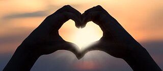 Zwei Hände formen ein Herz, durch das Sonnenstrahlen blinzeln.