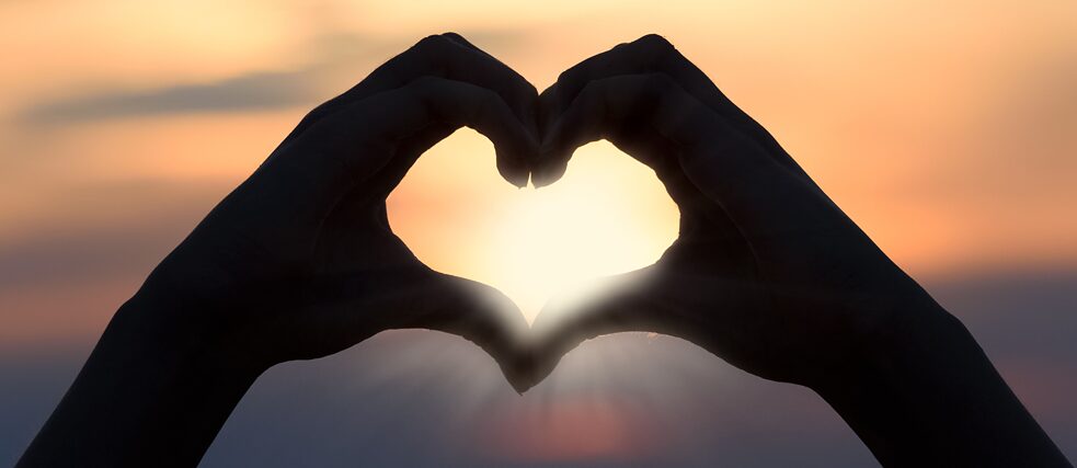 Zwei Hände formen ein Herz, durch das Sonnenstrahlen blinzeln.