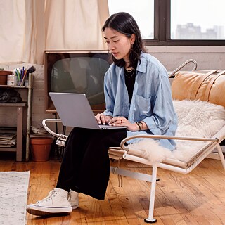 Junge Frau sitzt mit Laptop in einem Sessel in einem Wohnzimmer