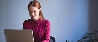 Eine Frau schreibt im Büro an einem Laptop und lächelt.