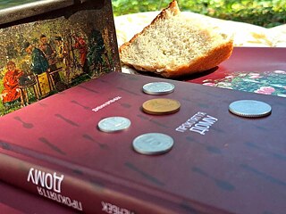 Книжка закрита, на ній лежать монети. Поряд стоїть ікона, на простирадлі лежить шматок хліба. 