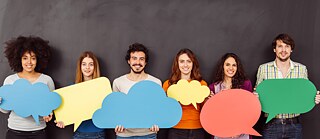 Rühm mehi ja naisi seisab üksteise kõrval tumeda seina ees ja hoiab enda ees suuri värvilisi kõnemulle. Neil on lõbus ja naeravad kaamerasse.