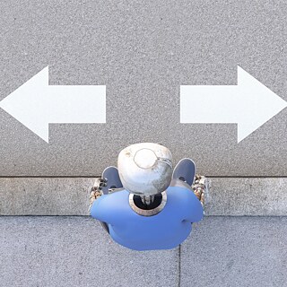 Ein Roboter steht auf der Straße, vor ihm zeigen ein Pfeil nach links und ein Pfeil nach rechts.