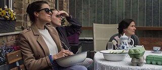 Ausschnitt aus Alle reden übers Wetter: Drei Frauen sitzen im Garten an einem Tisch und blicken in die Ferne.