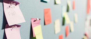 Bunte Notizzettel sind an einer Pinnwand befestigt. Einige Zettel sind beschriftet, andere leer.