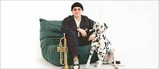 Le musicien de jazz luxembourgeois Daniel Migliosi est assis sur un canapé avec sa trompette et son chien.
