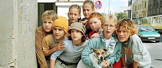 Fotoğrafta Emil ve dedektifler görülüyor. Toplamda sekiz çocuk ve bir köpek heyecanla bir şeye bakıyor. Berlin'de bir sokakta köşebaşında duruyorlar. Arkalarında Sophienstrasse görülüyor.