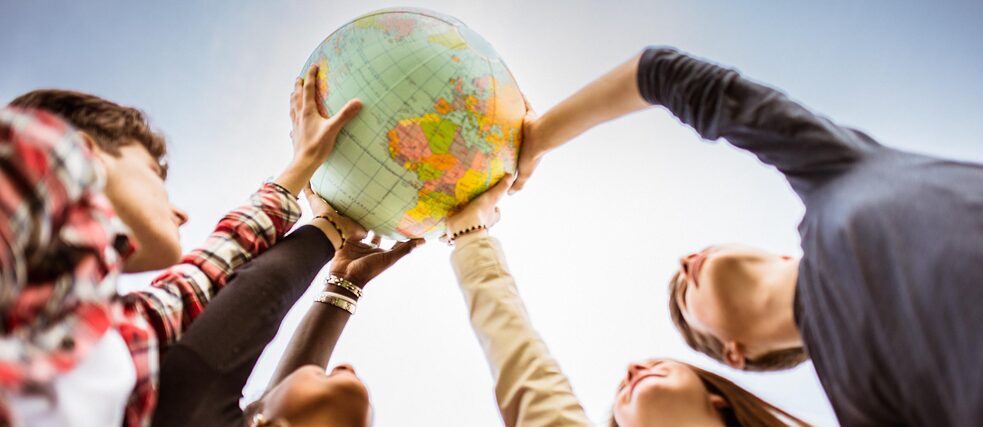 Several young people hold up a globe together