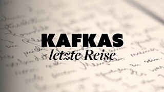 The image features the black inscription ‘Kafka's Last Journey’. In the background, there is a sheet of paper with handwritten text visible.