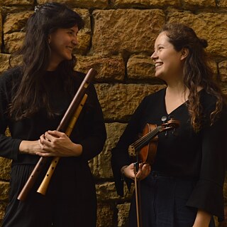 2 musiciennes se sourient devant un mur de pierres