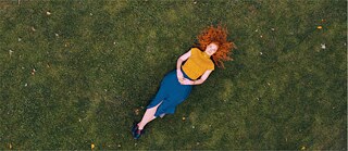 Höhenansicht: rothaarige Frau liegt auf einem Rasen