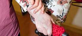Eine Pflegerin stützt eine ältere Dame, die mit einem Rollator geht