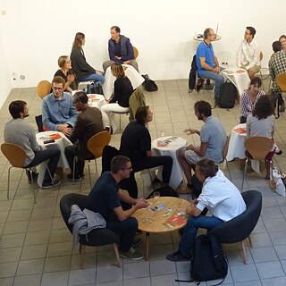 Dreiergruppen die um Tische sitzen und diskutieren