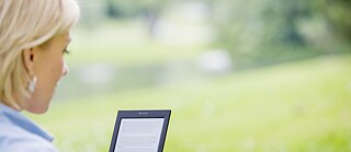 Жінка із електронною книгою на галявині влітку