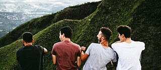  A group of four people sitting on a hill, smiling and looking at each other, with lush green hills in the background. © © Unsplash Chancenkarte: Your Pathway To Germany!