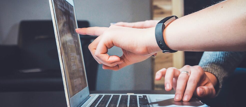 A person's hand with a fitness tracker on the wrist points to a graph on a laptop screen, while another hand types on the keyboard.
