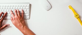 A person typing on a white keyboard, with a yellow wristwatch and a white computer mouse on the desk. © © Unsplash Job Hunting