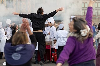 Auf dem Foto sieht man einen tanzenden Julien-Henry Vu Van Dung sowie zwei weitere tanzende Personen von hinten. Im Publikum sind einige Köche und Köchinnen erkennbar. 