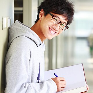 A young man wearing glasses holds a book during an interactive face-to-face language course.