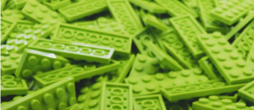 A close-up view of a large pile of bright green LEGO bricks, featuring various shapes and sizes, with the LEGO logo visible on some of the studs.