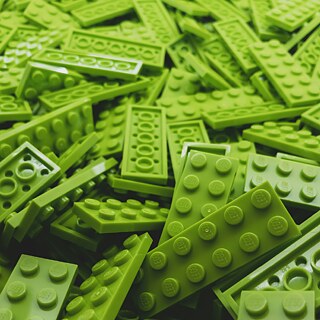 A close-up view of a large pile of bright green LEGO bricks, featuring various shapes and sizes, with the LEGO logo visible on some of the studs
