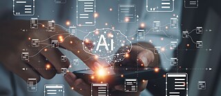 Sümboolne pilt tehisintellektist: käsi puudutab sõrmega nutitelefoni, esiplaanile ilmuvad erinevad sümboolsed sõnumid. Keskel on aju kujutis, millel on kiri „AI“, mis tähistab tehisintellekti.