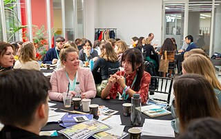 Personen sitzen an einem Tisch und diskutieren über verschiedene Unterlagen und Dokumente.