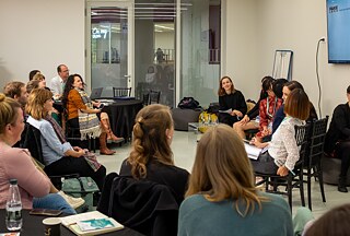 Several people sit on chairs in a room and interact with each other.