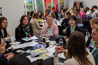 Several women sit at a table and discuss various papers and materials.