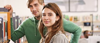 Schüler in der Bibliothek vor einem Bücherregal