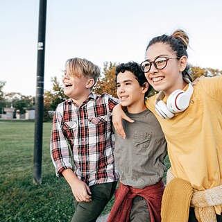 Drei Kinder laufen fröhlich, Arm in Arm, einen Weg entlang.