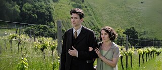 Filmszene mit Franz Kafka und Dora Diamant die Arm in Arm an einem grünen Feld vorbeilaufen 