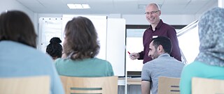 A counsellor speaks in front of a group of people who can be seen sitting on chairs from behind.