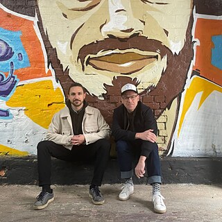 Der Bassist Simon Fagerstedt und der Schlagzeuger Peter Krutsch vor einer besprühten Steinmauer.