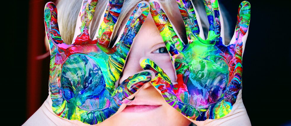 Дитина тримає перед обличчям розмальовані яскравими фарбами руки.