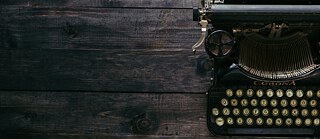 A close-up of a vintage Corona typewriter with round keys, placed on a dark wooden surface, showcasing its classic design and mechanical details. © © Unsplash Vintage Corona Typewriter on Wooden Surface