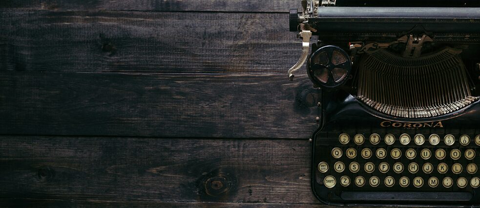 A close-up of a vintage Corona typewriter with round keys, placed on a dark wooden surface, showcasing its classic design and mechanical details.