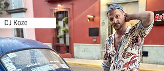 DJ Koze in bunter Kleidung neben einem alten VW Käfer