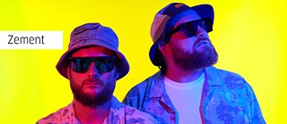 Zement, zwei Männer vor einem gelben Hintergrund