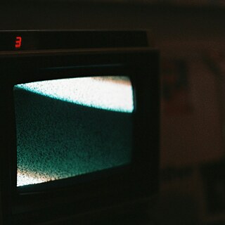 Ein alter Fernseher mit einem grünlichen Bildschirm, der statisches Rauschen anzeigt, in einem dunklen Raum.