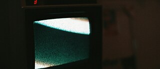 An old television with a greenish screen displaying static noise in a dark room. © © Unsplash Old Television with Static Noise