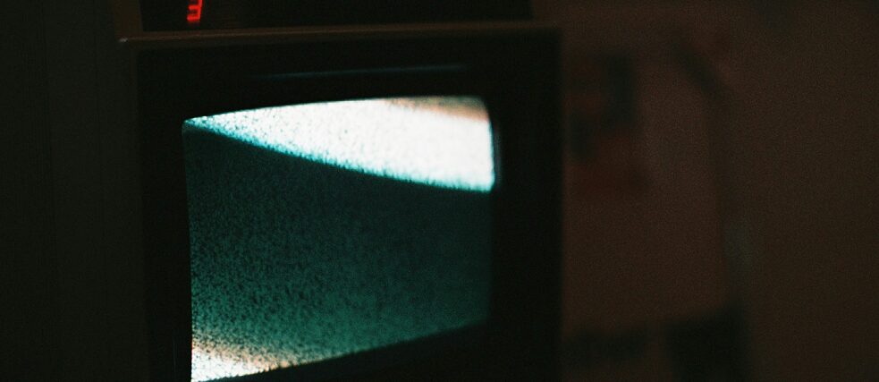 An old television with a greenish screen displaying static noise in a dark room.