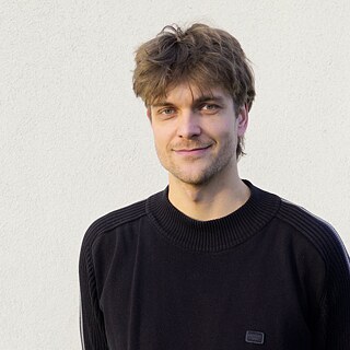 Portreefoto kirjanik Markus Thielemannist. Tal on lühikesed pruunid juuksed, hallid silmad, kolmepäevane habe ja ta naeratab kergelt kaamerasse.