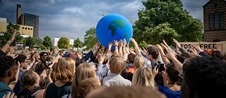 Viele Menschen strecken die Hände zur Erdfigur hin.