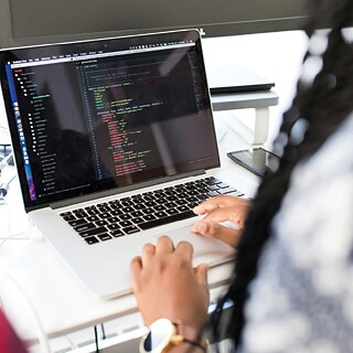 Person tippt auf einem Laptop, auf dem Code zu sehen ist.