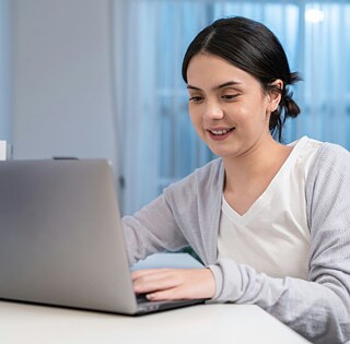 Mädchen sitzt am Schreibtisch vor ihrem Laptop und folgt ihrem Online-Deutschkurs