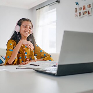  A girl wearing headphones sits at a desk, focused on her laptop while engaged in her study.