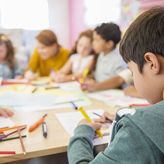 A group of children sitting at a table, focused on their artwork with pencils and paper in front of them.