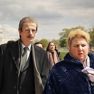 Grupo de personas caminando al aire libre con el edificio del Capitolio de los Estados Unidos de fondo en un día nublado. Vestimenta formal.
