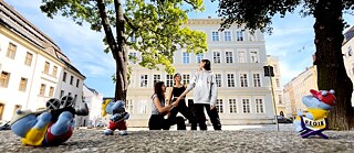 Úryvek ze scény filmu: Tři školačky a tři postavičky Happy Hippo stojí na náměstí.